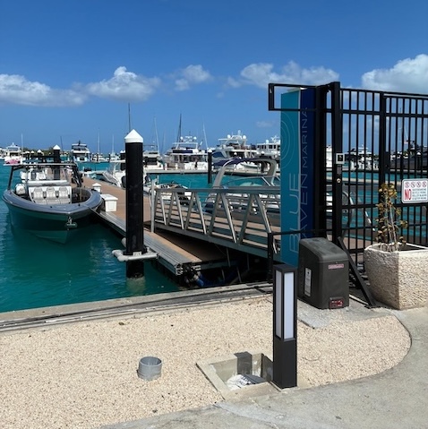 The image shows the secure entrance point to the marina deck, featuring modern docking facilities and boats in vibrant turquoise water.